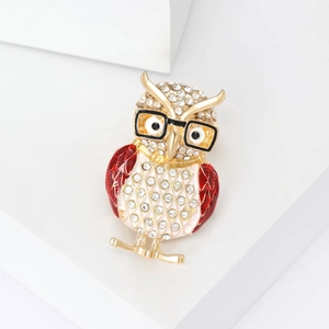 Sparkling crystal owl brooch with glasses and red enamel wings on white pedestal