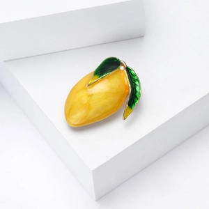 Cute mango shaped enamel brooch pin with yellow fruit and green leaf on white pedestal