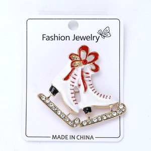 Detail of white enamel ice skate brooch with red bow and gold blade on card