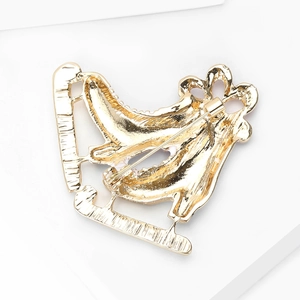 Detail view showing the golden metal back structure and safety pin of the skate brooch