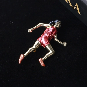 Broche athlète en émail rouge et plaqué or posée sur un fond de velours noir