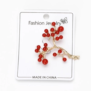 Detail of holly berry branch brooch with red beads on gold plated alloy and white card