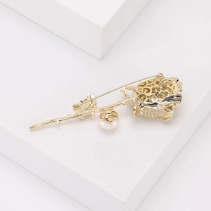 Détail de broche rose dorée avec zircons, perle et épingle de sûreté sur fond blanc épuré