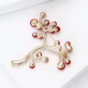 Vintage gold holly branch brooch with red berries and safety pin clasp on white background