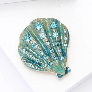 Macro detail of teal enamel shell brooch with gold grid and light blue rhinestones