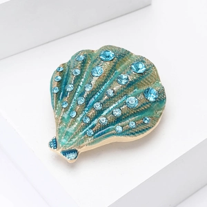 Detailed close-up of shell-shaped brooch with teal enamel and sparkling blue rhinestones