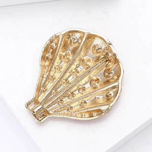 Macro detail of the back view of the golden shell brooch showing the secure pin closure
