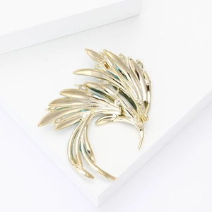 Close-up of golden phoenix wing brooch with blue crystals on white geometric stand