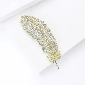 Detailed close-up of a sparkling gold leaf brooch with crystals on white pedestal