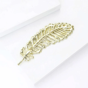 Detail shot of golden feather brooch with intricate metal texture on white pedestal