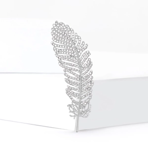 Detail of silver feather brooch with sparkling crystals on minimalist white background