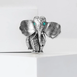 Vintage silver elephant brooch with green crystal eyes on a white minimalist stage