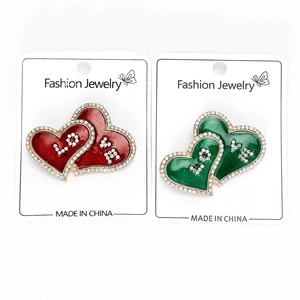 Detail of heart-shaped alloy brooches with red and green enamel and crystal rhinestones
