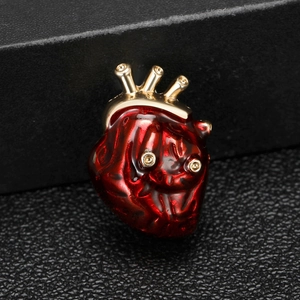 Détail macro d'une broche cœur anatomique en émail rouge et finitions métalliques dorées