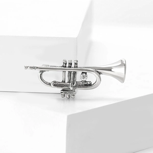 Detailed close-up of a silver trumpet brooch with sparkling crystal on a white background