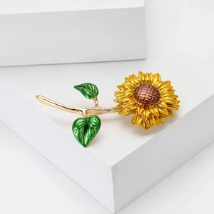 Broche tournesol en émail jaune avec feuilles vertes et tige dorée sur décor blanc