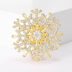 Macro shot of gold snowflake brooch with yellow trapezoid crystals on white surface