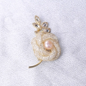Détail de la broche rose dorée en maille avec perle rose et strass marquise brillants
