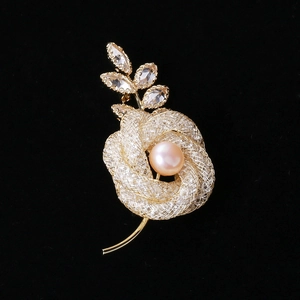 Détail d'une broche rose en maille dorée avec perle rose et strass marquise scintillants