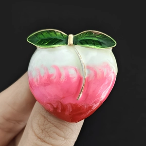 Gros plan d'une broche en émail pêche brillant avec feuilles vertes sur fond noir