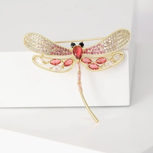 Elegant gold dragonfly brooch with pink and red cubic zirconia on a white platform