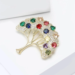 Détail d'une broche arbre dorée avec pierres multicolores et cristaux sur socle blanc