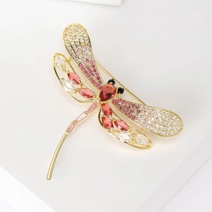Elegant gold dragonfly brooch with pink micro-set crystals on white geometric stand