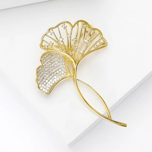 Macro detail of ginkgo leaf brooch with pave-set zircons on white podium