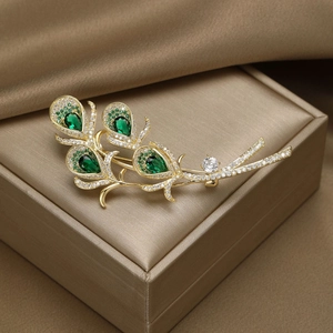 Macro detail of gold plated peacock feather brooch with green crystals on silk background