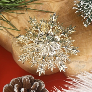 Golden multi-layer snowflake brooch with sparkling zircons on a wooden winter background