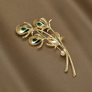 Elegant gold flower brooch with green drop crystals and zircon pavé on silk background