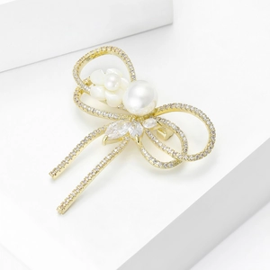 Broche nœud élégante en or avec zircons, fleur en nacre et perle sur un piédestal blanc