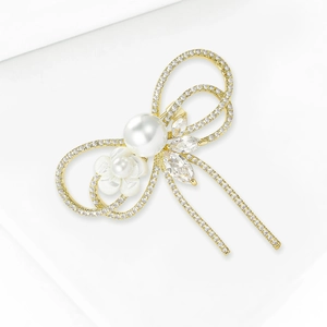 Élégante broche nœud dorée avec cristaux, grande perle blanche et détail de fleur de camélia