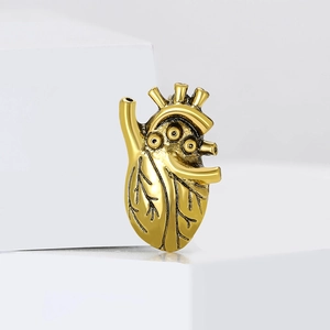 Vintage gold anatomical heart brooch with detailed vascular structure on white podium