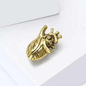 Vintage gold anatomical heart brooch in creative alloy design on a minimalist white stand