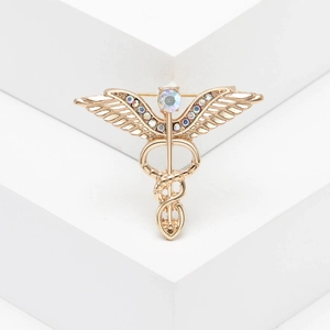 Golden Caduceus angel wing brooch with colorful crystals on a geometric stand