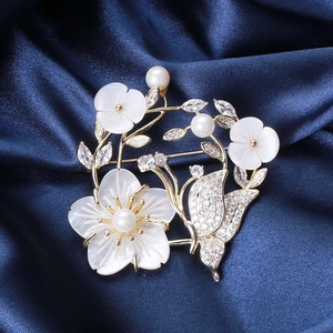 Détail d'une broche fleur en nacre et papillon avec perles sur velours bleu nuit