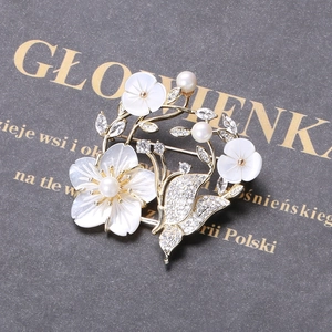 Détail macro de broche fleur en nacre avec papillon en zircon et perles fines