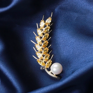 Makroaufnahme der goldenen Weizenbrosche mit gelben Zirkonia und Perle auf blauer Seide