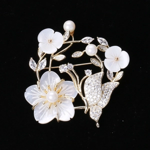 Gros plan détaillé d'une broche fleur en nacre avec perles et papillon en zircon