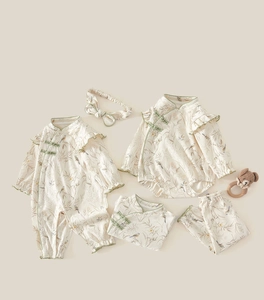 Flat lay of Chinese style cotton infant romper set with bird prints and a bear rattle