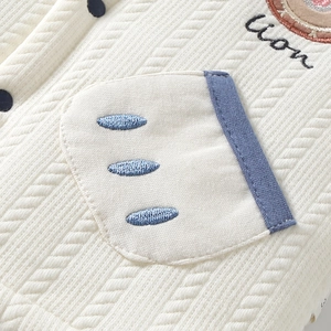 Détail macro d'un cardigan bébé montrant la broderie lion et la maille gaufrée