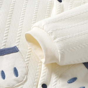 Détail macro de tricot pour bébé blanc avec poignet côtelé et broderie d'œil bleu