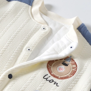 Détail de cardigan matelassé pour bébé avec broderie de lion et boutons-pression