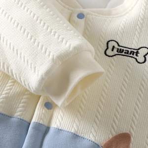 Detail van gebreid babyvestje met borduursel en lichtblauwe drukknoopjes