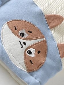 Dik gebreid babyvestje in lichtblauw met gedetailleerd borduursel van een cartoon dier