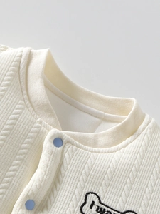 Gebreid babyvestje in crème met twill-textuur en blauwe drukknopen voor jongens
