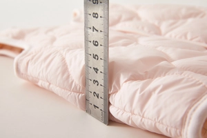 Close-up of pink quilted puffer vest showing 2.5cm thickness with a measuring ruler