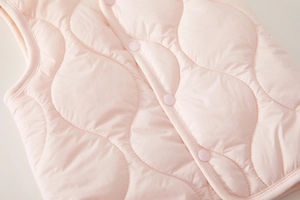 Detail of pink quilted baby vest with wavy stitching and high-quality resin snap buttons