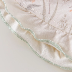Détail du bonnet en coton pour bébé avec motif floral et bordure verte ondulée délicate
